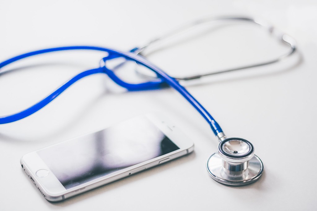 A blue stethoscope rests beside a white smartphone on a light surface