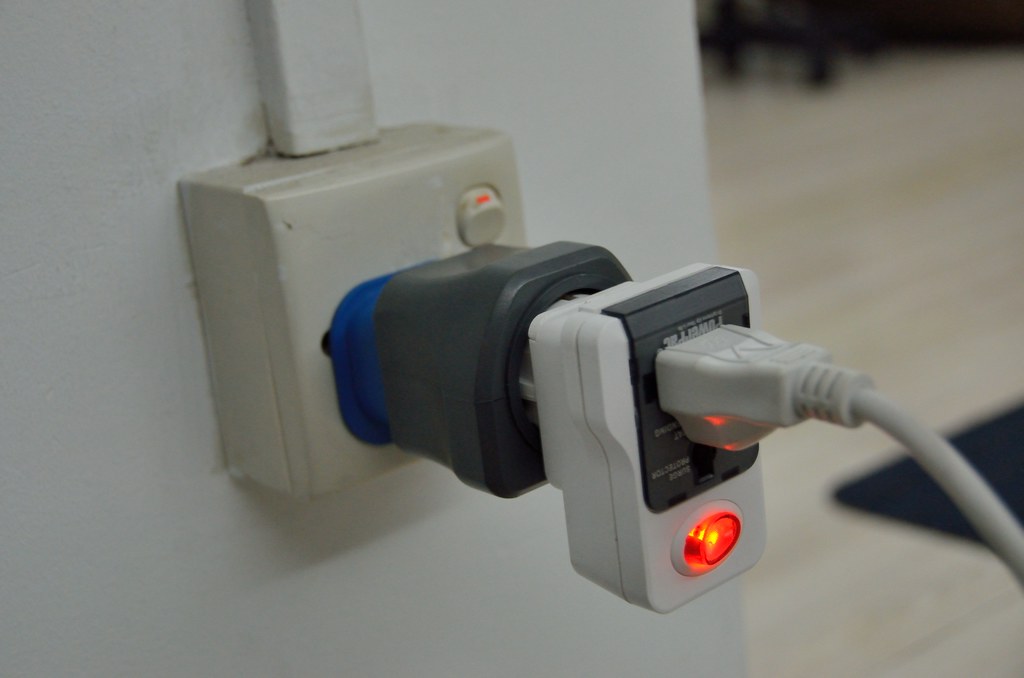 Three travel plug adapters stacked into one wall socket, with a power cable plugged into the last one