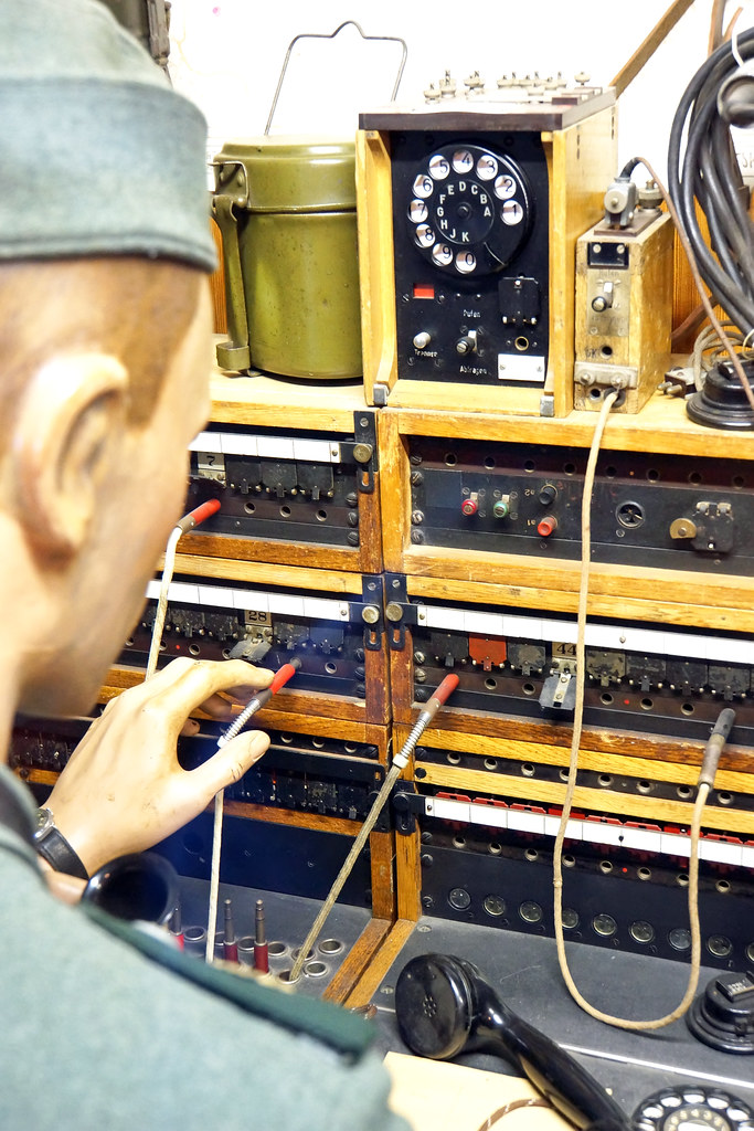 Operator plugging cables into a wooden telephone switchboard with a rotary phone on top