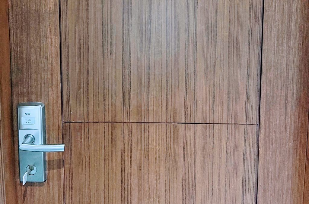 A hotel room door with a silver key card lock and lever handle set into a wood-grain panel
