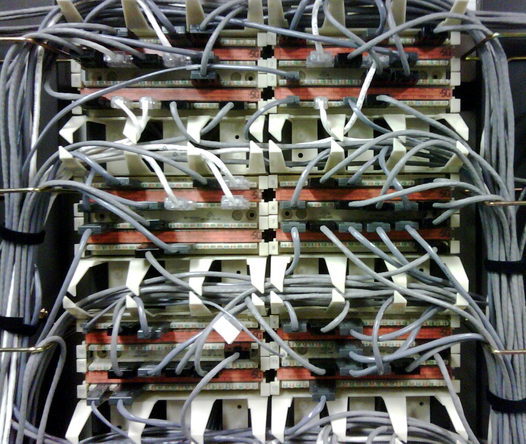 Dense grey network cables looping into a rack of patch panels, many connections routed through one point