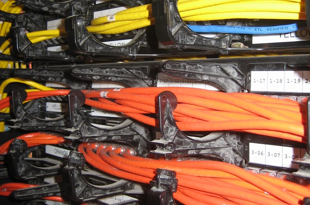 Bundles of yellow and orange network patch cables routed through black cable managers on a numbered patch panel