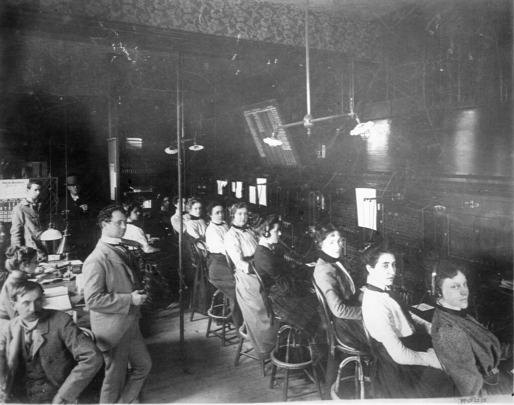 Rows of telephone switchboard operators in 1900, each patching calls between many lines by hand